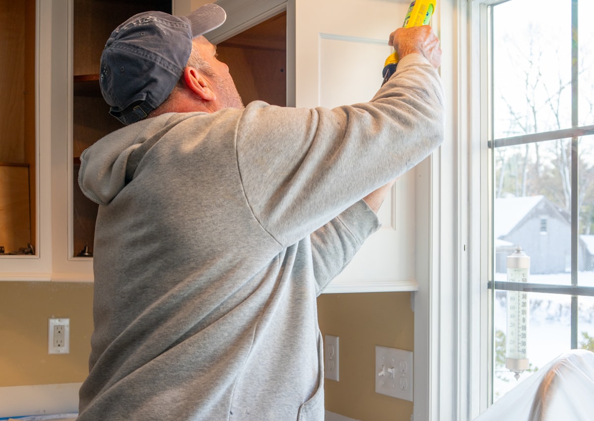 Window fitter applying sealant around a newly installed frame with dust sheets down